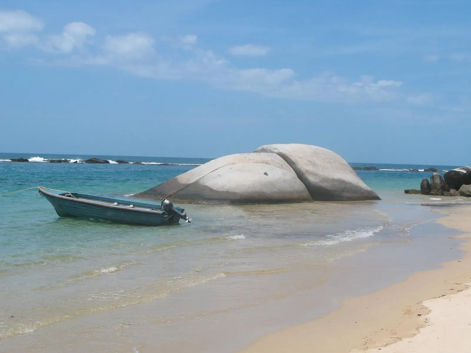 A fishing boat anchored beside a giant rounded boulder at La Piscina cove in Tayrona National Park