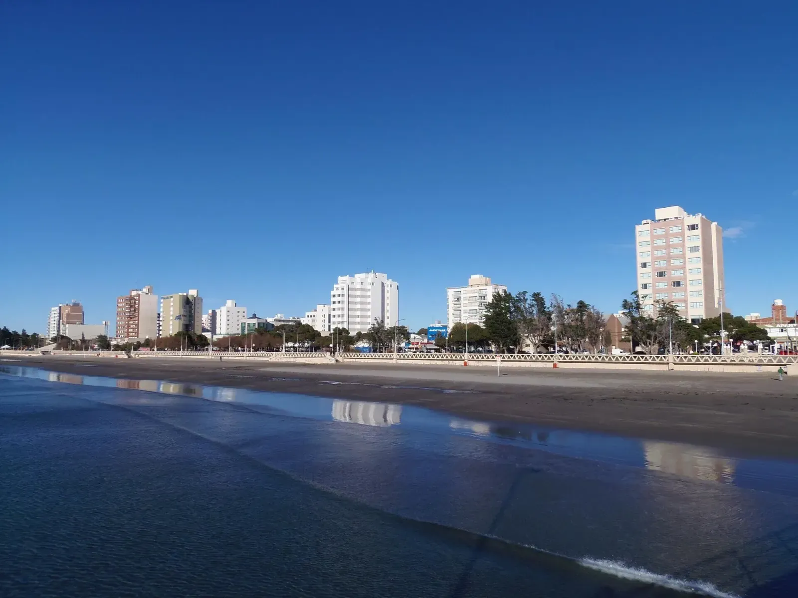 City skyline of Puerto Madryn reflected in wet sand along the Golfo Nuevo shore