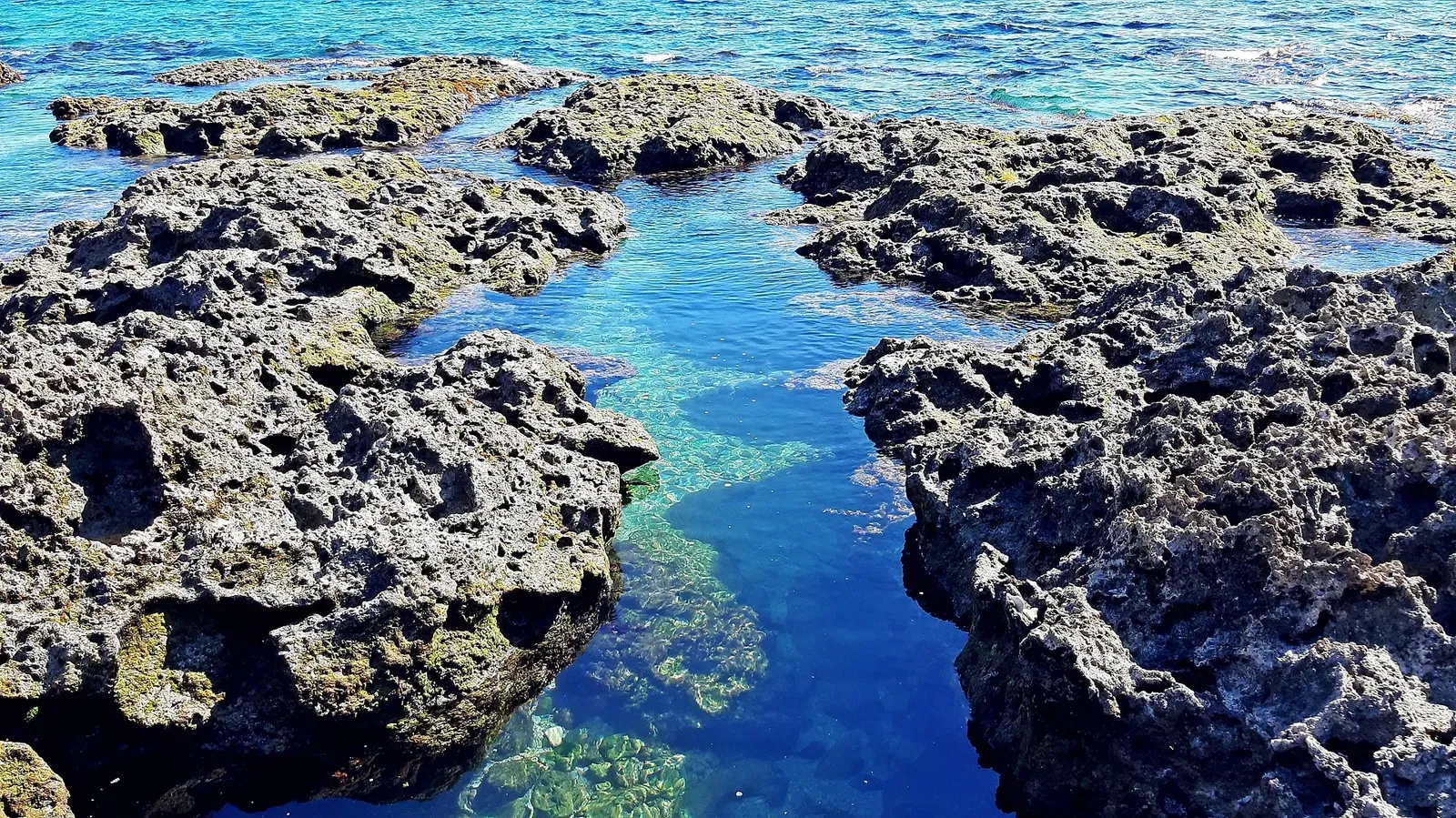 A narrow channel of clear blue water cuts through coral-rock coastline at Siangjiao Bay.