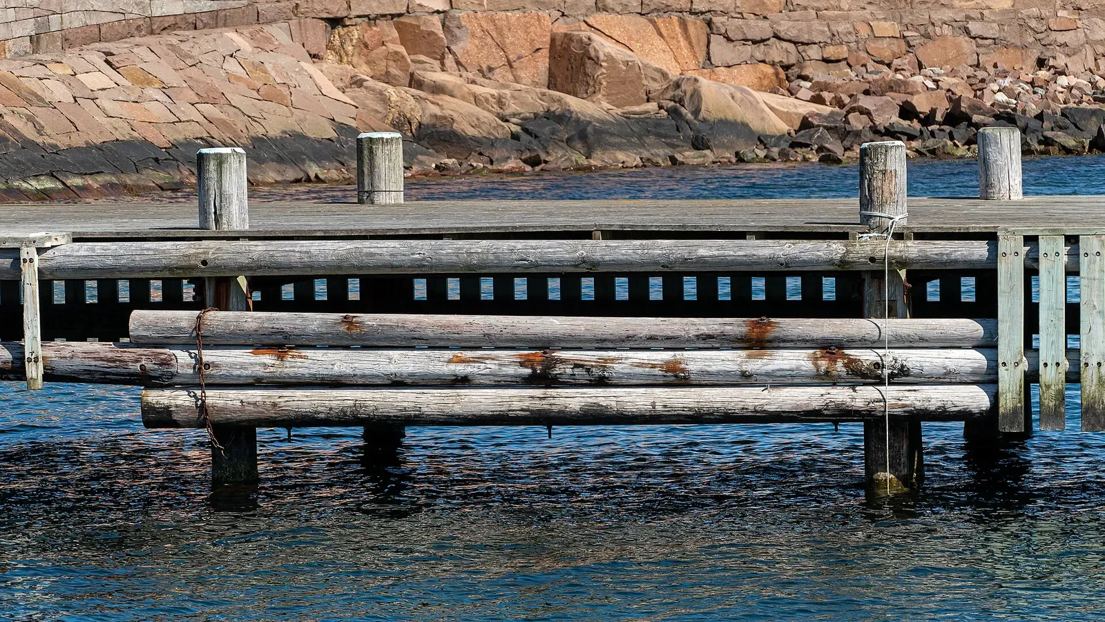 A wooden jetty in Kyrkevik harbor backed by pink Bohuslän granite
