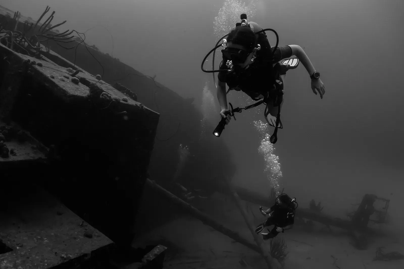 Two divers with torches exploring the sunken freighter Hilma Hooker in black and white