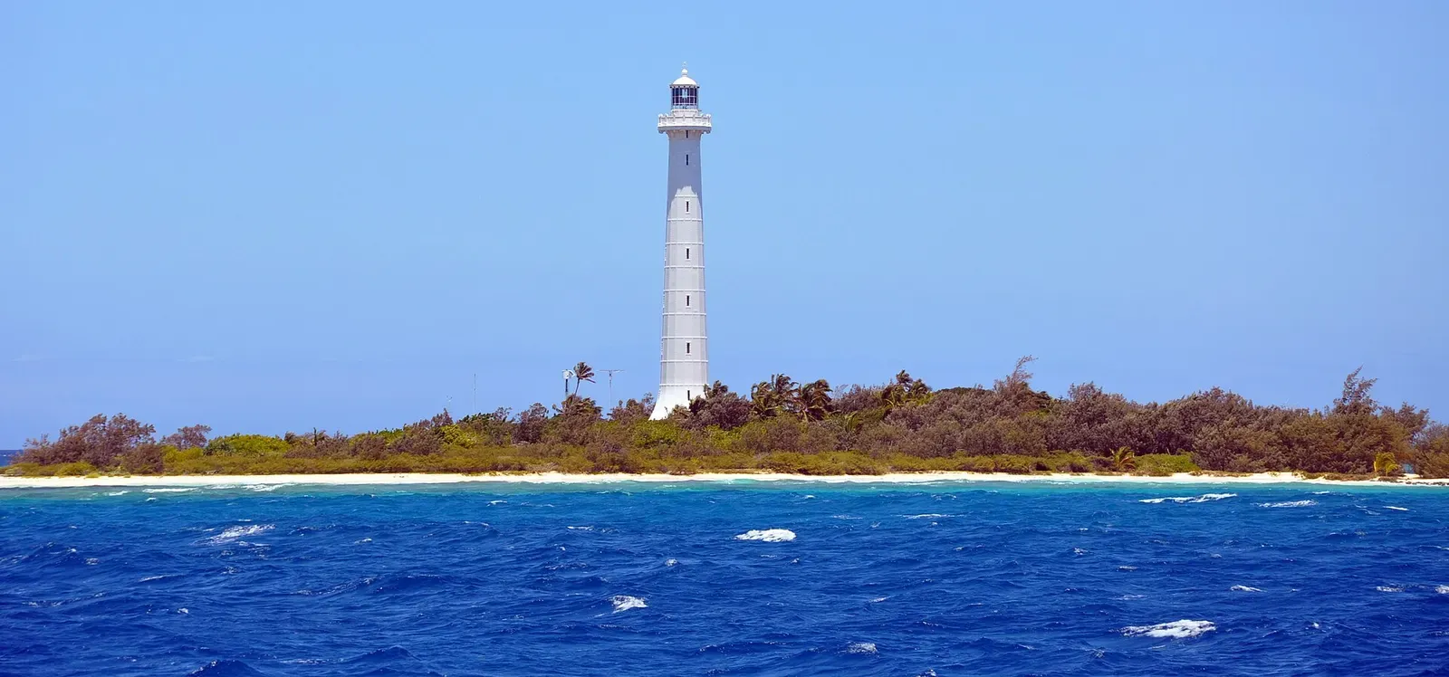 The white Amédée lighthouse rising above the islet's reef, seen from the water