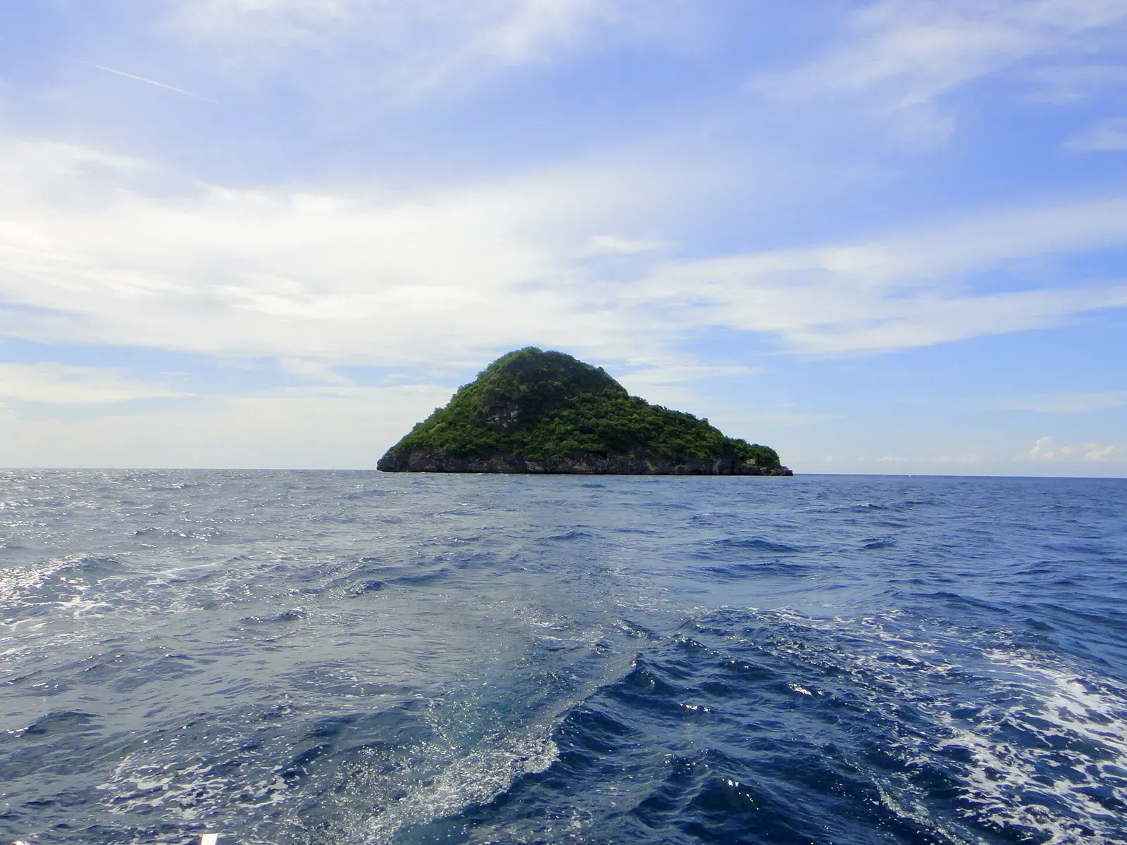 A dive boat's wake trails toward the small forested limestone islet of Gato near Malapascua.