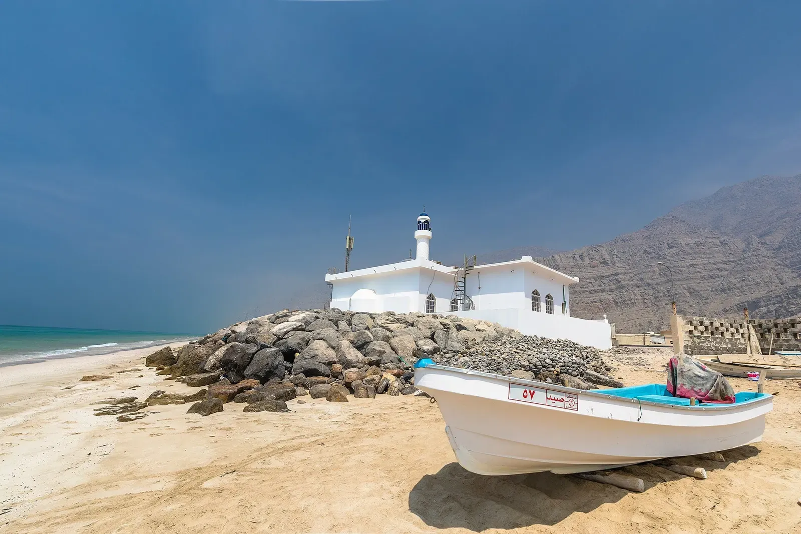 A whitewashed lighthouse stands above a pebble beach on the Musandam coastline near Khasab