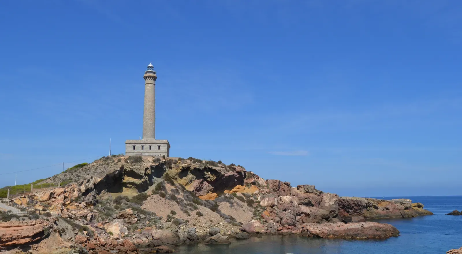 Cabo de Palos lighthouse standing on a rocky headland above a calm cove