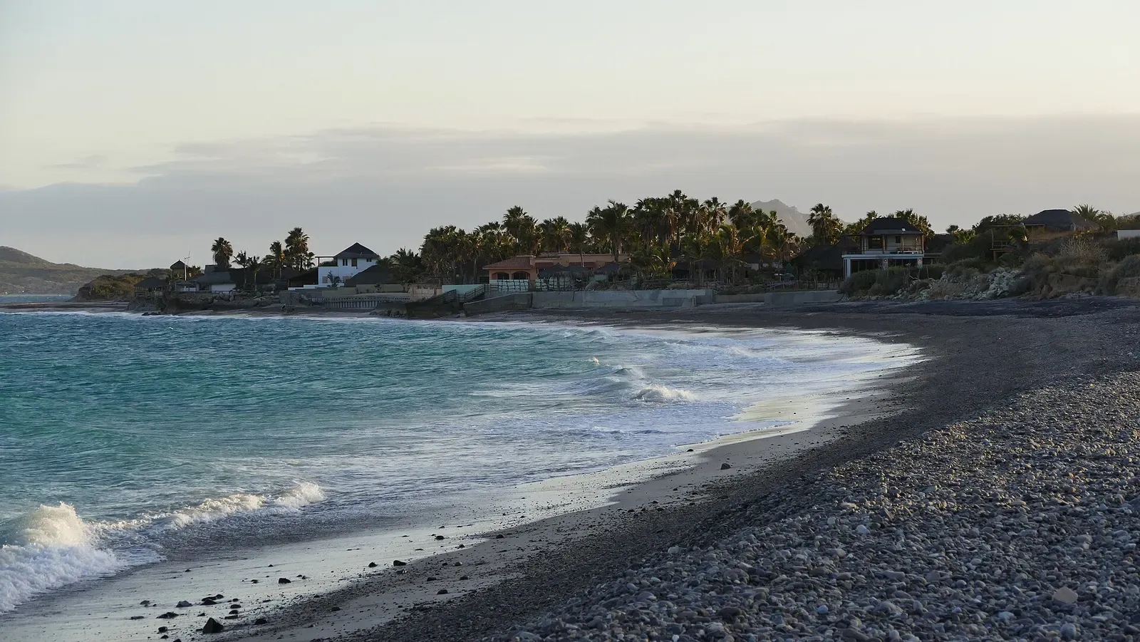Waves break along the pebble beach at Cabo Pulmo with a mountain backdrop