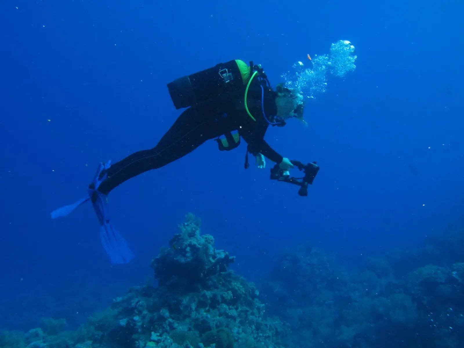 A diver trailing bubbles glides over open blue water near Gota Kebir
