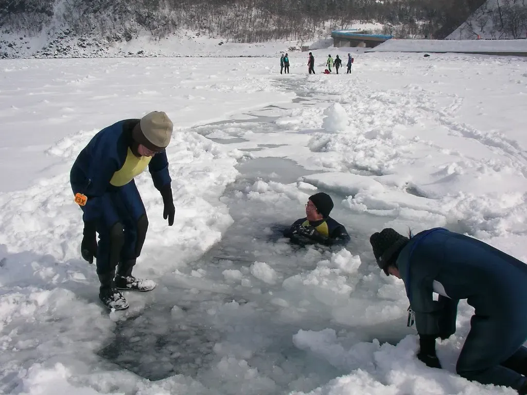 A drysuited person floats in a pool of open water cut into the sea ice while two others look on from the edge