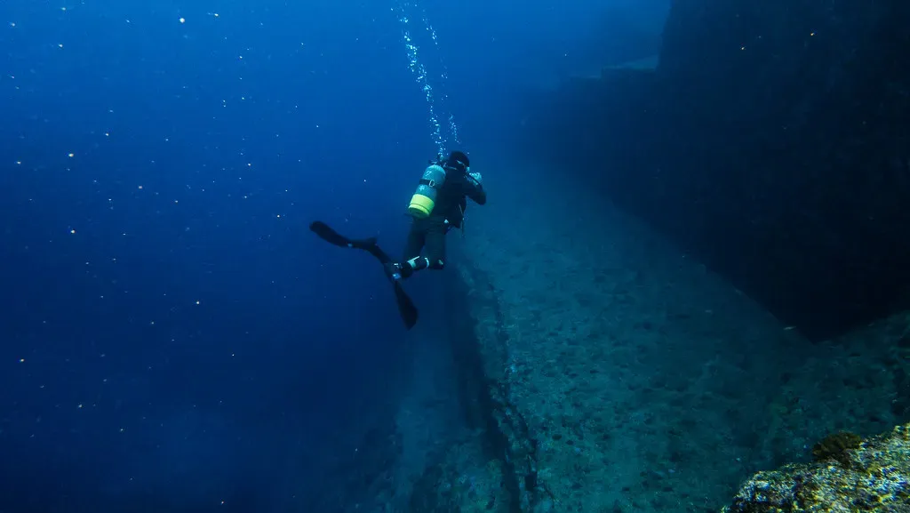 A diver hovers over stepped rock terraces near the Yonaguni Monument dive site.