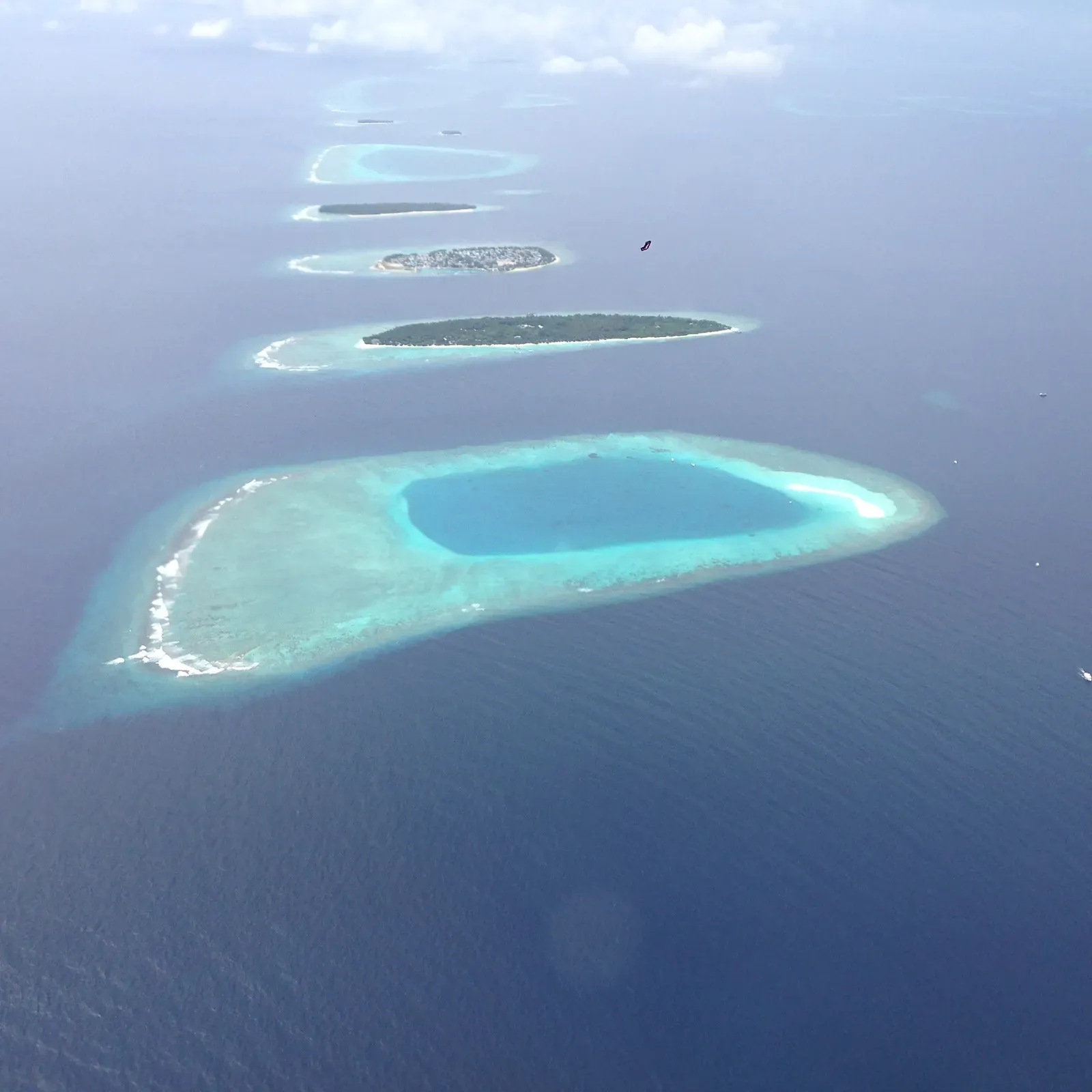 Aerial view of a chain of reef islands enclosing a shallow turquoise lagoon