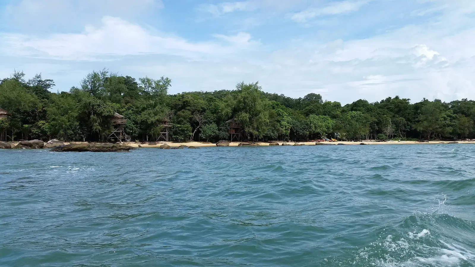 Tree-lined shoreline with stilted huts seen from the water near Koh Rong