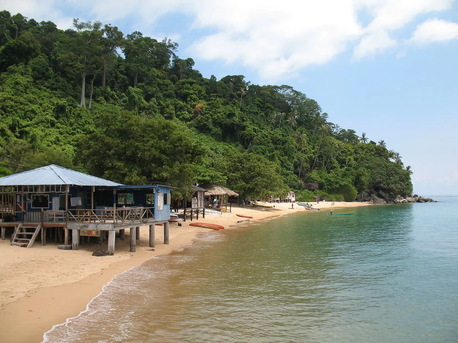 A quiet sandy beach lined with wooden huts beneath Tioman's jungle-covered hills