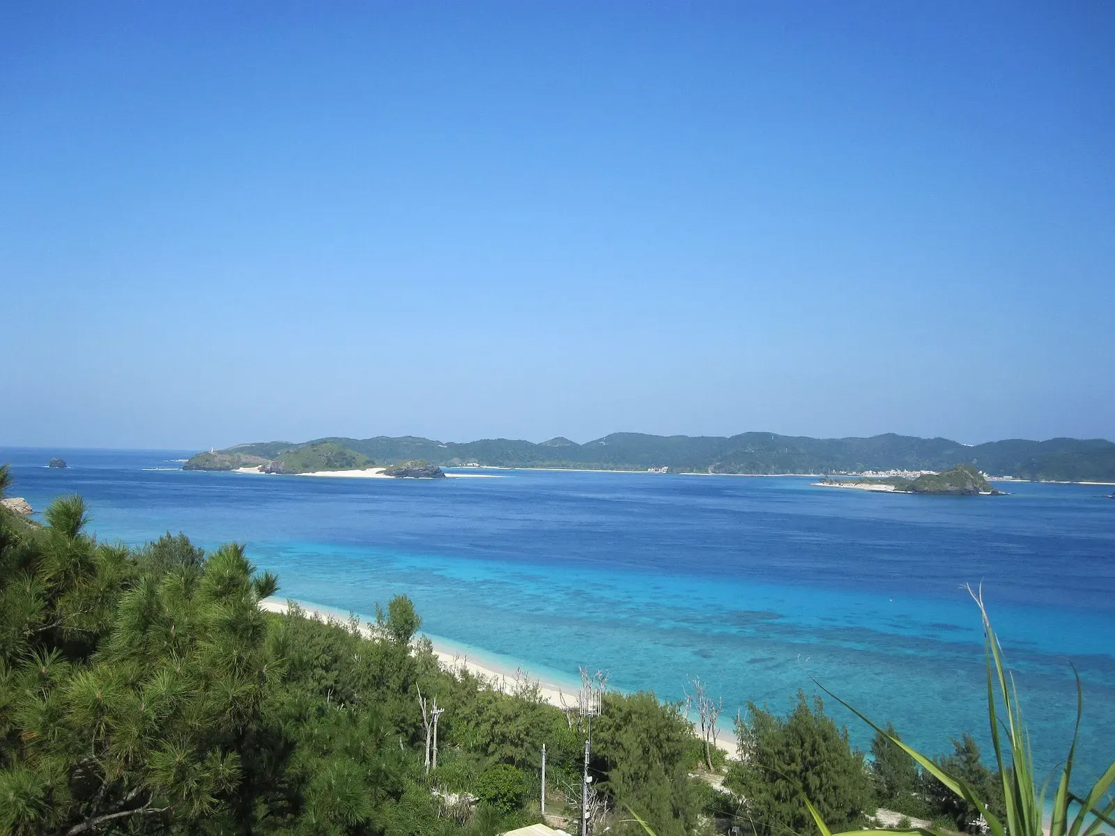 White sand curves into pale turquoise shallows below a green headland on Aka Island.