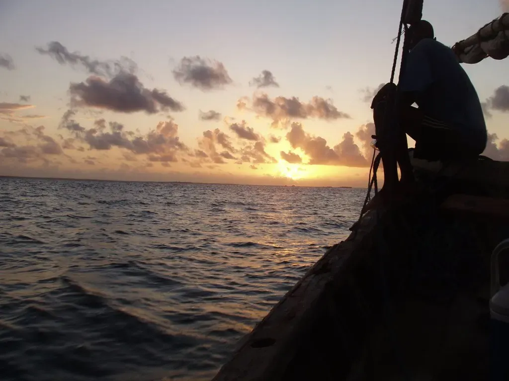 A fisherman sits in silhouette on a dhow as the sun sets over the water off Mafia Island