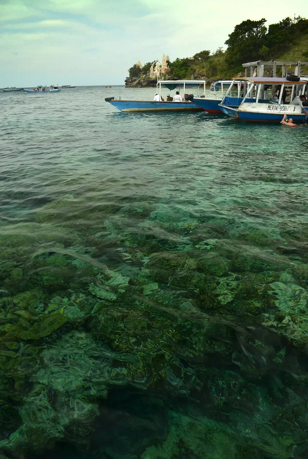 Dive boats moored in clear turquoise water off a temple point on Menjangan Island