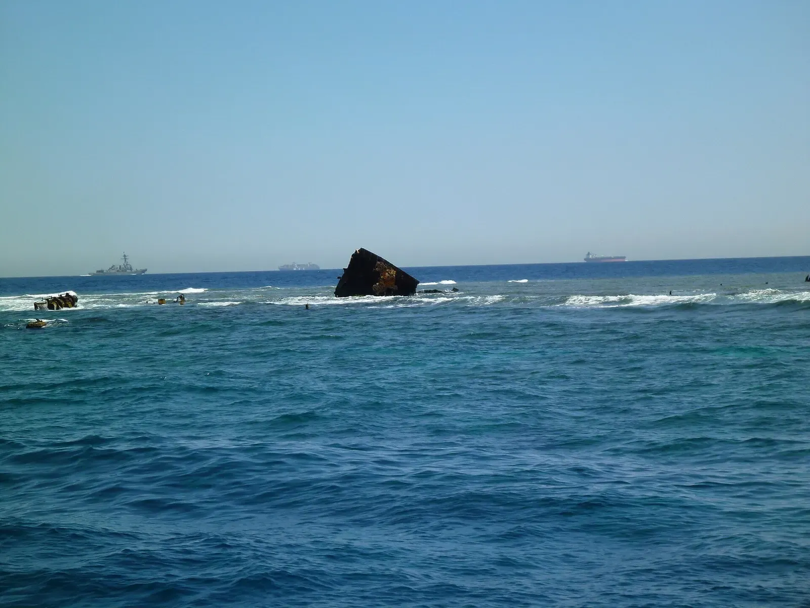 The wreck of the Kimon M breaks the surface at Abu Nuhas reef, with ships passing in the shipping lane beyond.